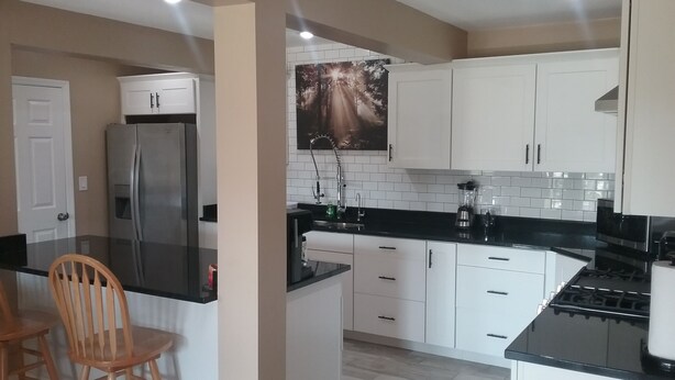 Eine moderne Küche mit weißen Schränken, einer schwarzen Arbeitsplatte und einem Edelstahl-Kühlschrank.