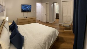 Une chambre à coucher avec un lit, un téléviseur fixé au mur, une commode et une chaise.