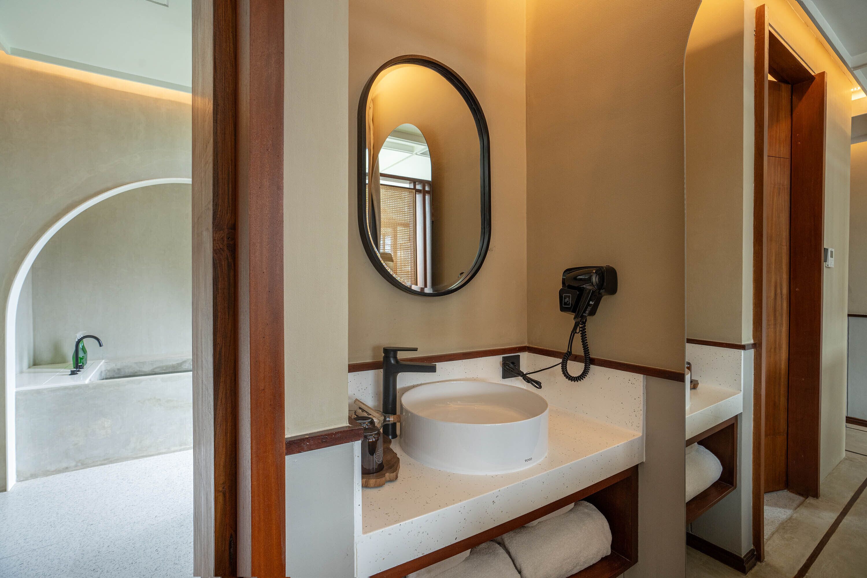 A bathroom with a round white sink, a mirror, and a hairdryer.