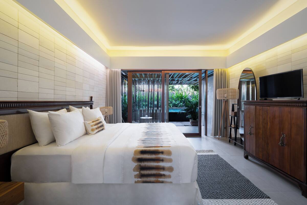 A hotel room with a large bed, a television, a cabinet, and a view of the outdoors.