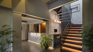 A modern interior with a reception desk, a staircase with illuminated steps, and potted plants. - The Kemilau Hotel & Villa Canggu (Tibubeneng)