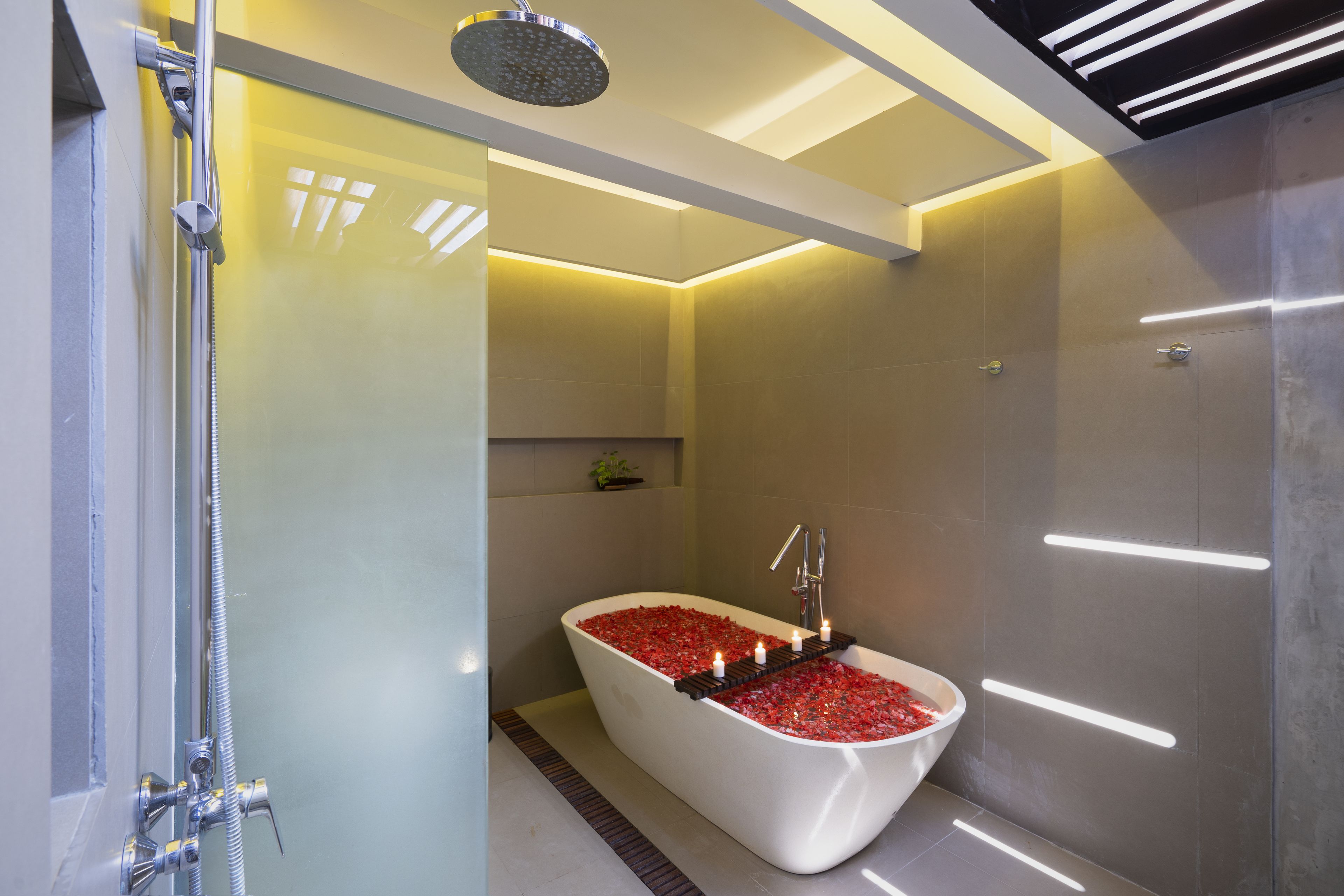 Une salle de bain moderne avec une baignoire îlot remplie de petits galets rouges, une pomme de douche et un éclairage encastré.