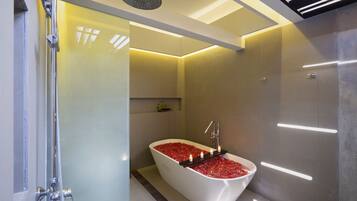 Une salle de bain moderne avec une baignoire îlot remplie de petits galets rouges, une pomme de douche et un éclairage encastré.