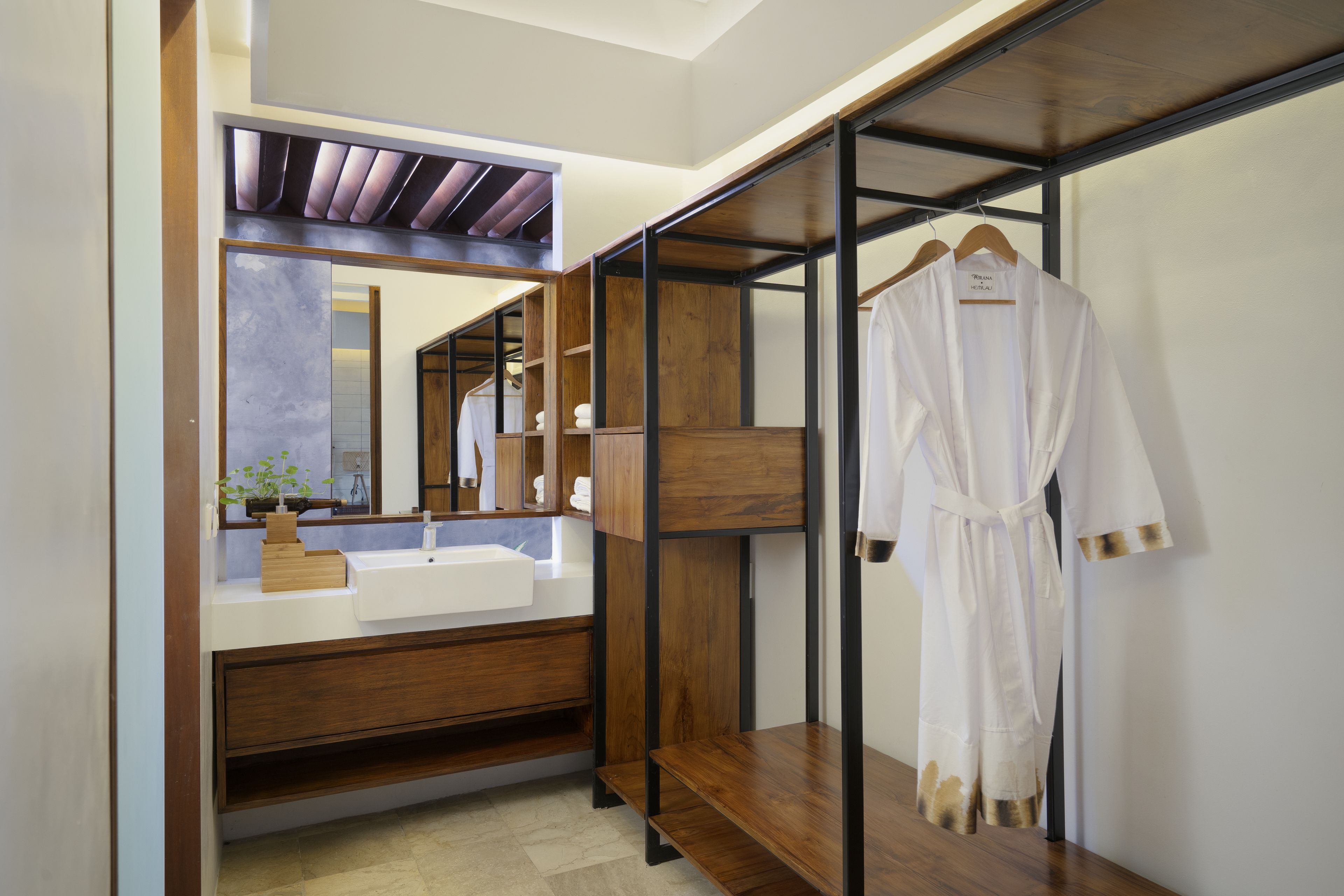 A modern bathroom with a wooden vanity, a large mirror, and a robe hanging on a rack.