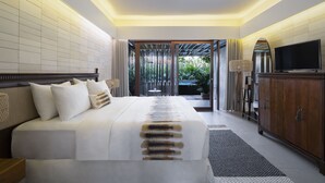 A hotel room with a large bed, a television, a wooden cabinet, and a view of a garden through a sliding door. - The Kemilau Hotel & Villa Canggu (Tibubeneng)