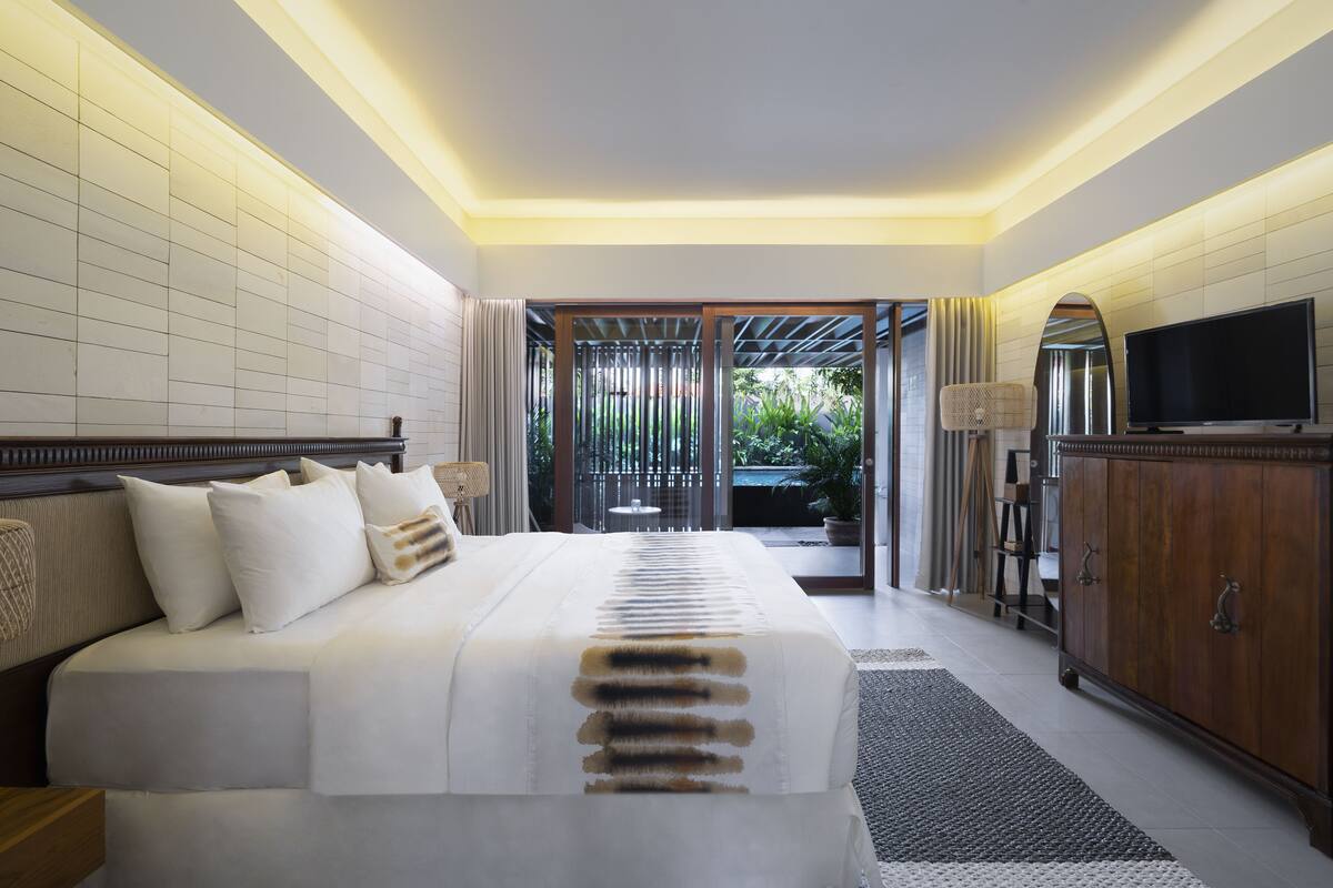 A hotel room with a large bed, a television, a cabinet, and a view of the outdoors.
