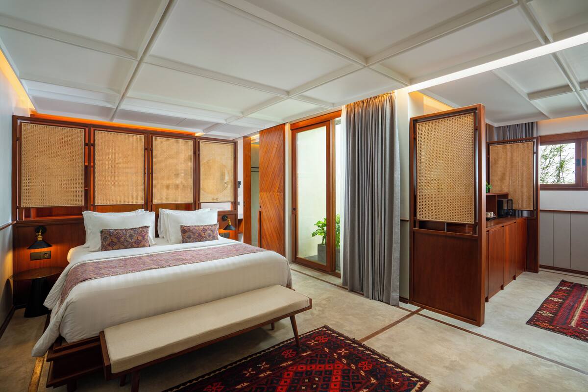 A hotel room with a large bed, a bench, a desk, and a view of the outdoors.
