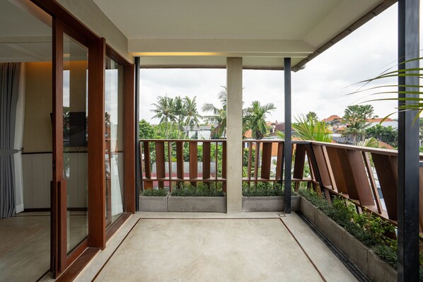 A balcony with a view of palm trees and houses, a concrete floor, and a wooden railing.