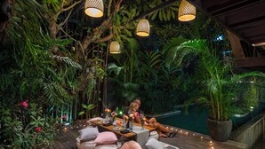 An outdoor dining area with a pool, surrounded by lush greenery and hanging lights. - The Kemilau Hotel & Villa Canggu (Tibubeneng)