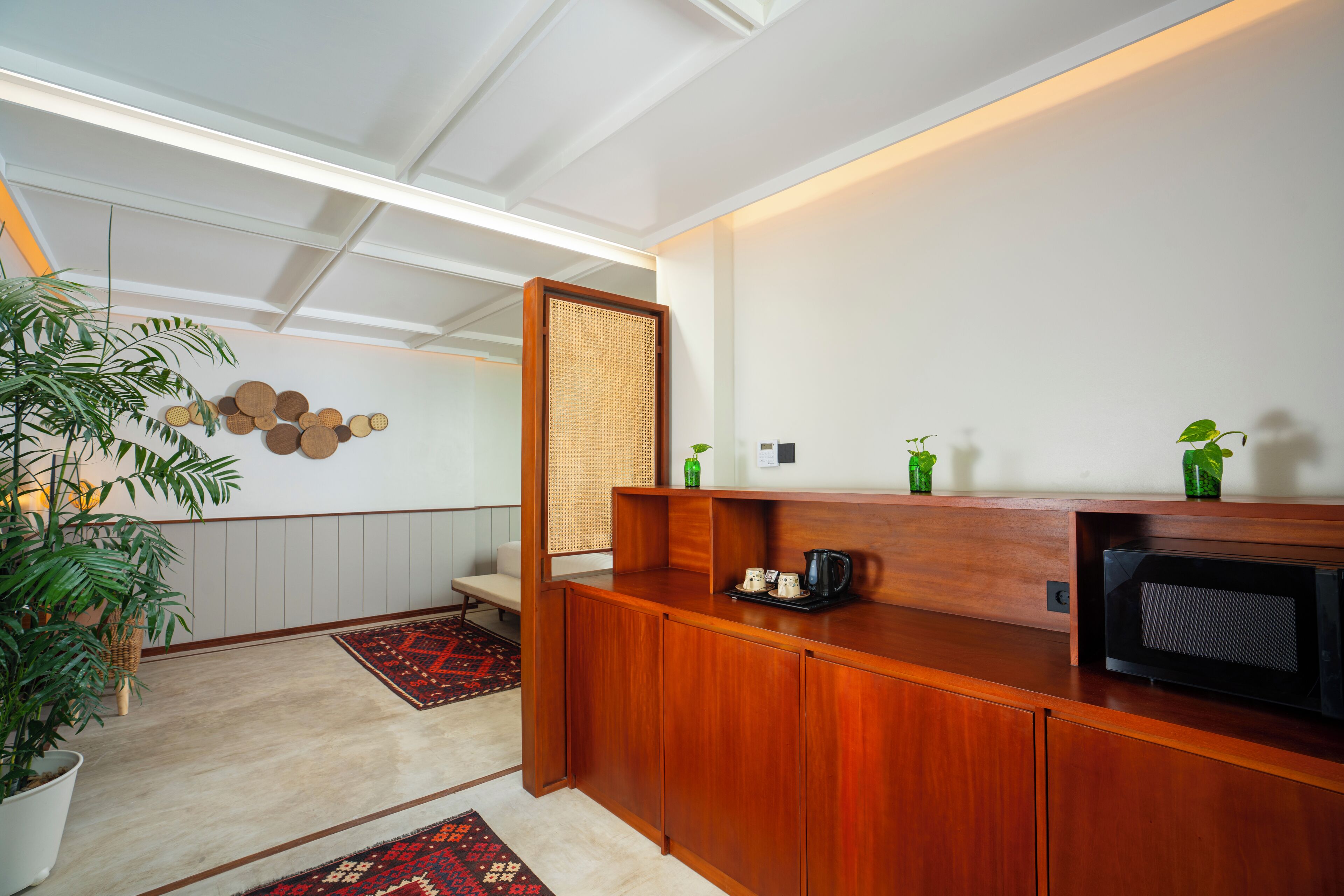 Una cocina moderna con encimera de madera, microondas y cafetera. Hay una planta en la encimera y una pared con un panel de madera decorativo.