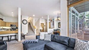 Ein modernes Wohnzimmer mit einer grauen Eckcouch, einer Küche mit Holzausstattung, einem Essbereich und einer Treppe zu einer weiteren Ebene.