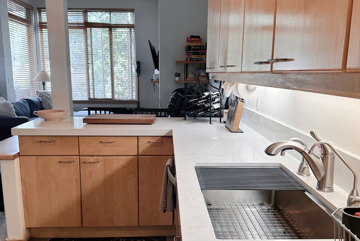 Una cocina con armarios de madera, una encimera, un fregadero con rejilla y una ventana con persianas.
