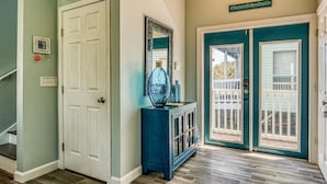 A hallway with a white door, a blue console table with a mirror, and a teal door leading to a balcony.