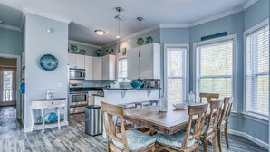 A modern kitchen with white cabinets, a central island, and a dining area with wooden chairs and a table.