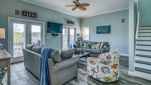 A spacious living room with a gray sofa, a patterned armchair, and a ceiling fan.