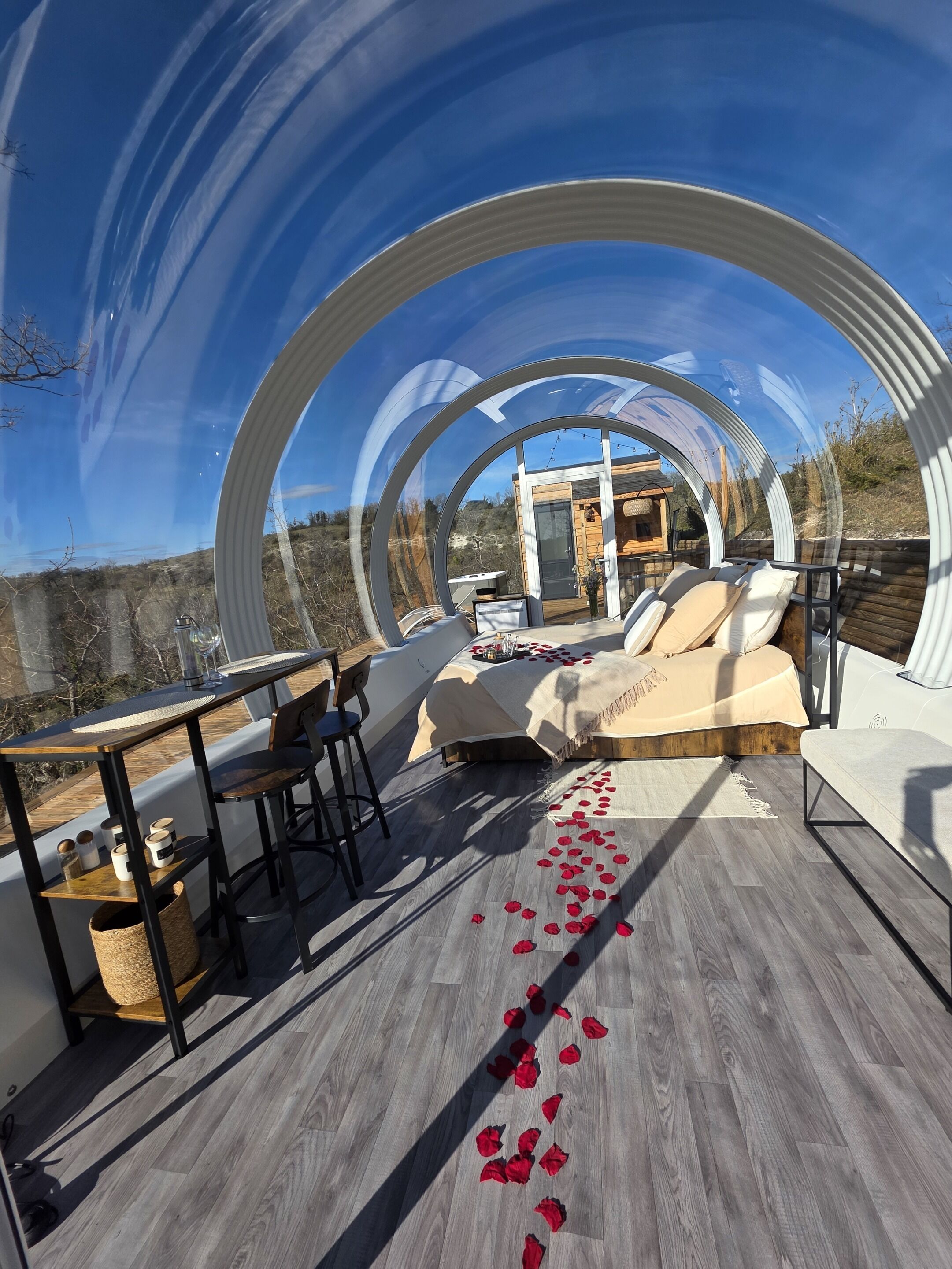 Una estructura tipo cúpula transparente con una terraza de madera, un sofá y una mesa con sillas.