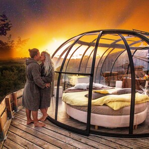 A couple embracing inside a dome-shaped structure with a bed and a table visible inside. - Les Gouttes D'eau (Labastide-de-Penne)