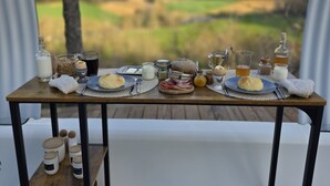 Une table  à manger dressée avec divers plats et accompagnements, placée sur un balcon d’où l’on peut admirer un paysage rural.