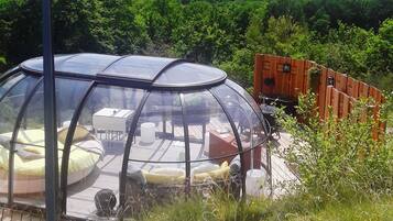 A transparent dome structure with a table and chairs inside, surrounded by a wooden deck and a wooden fence.