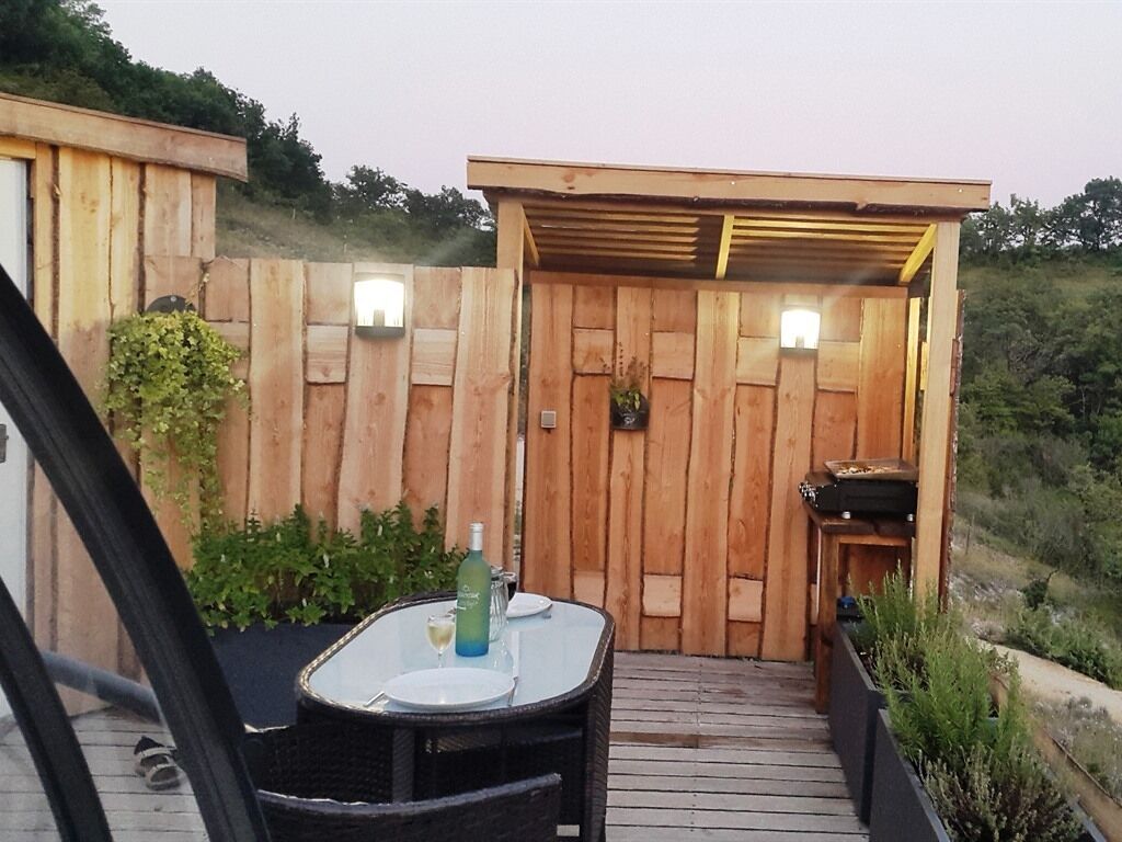 Une terrasse en bois avec une table et des chaises, une clôture en bois et une petite construction dotée d’un toit.