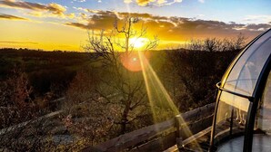 Une vue sur le coucher de soleil, prise depuis une structure entièrement vitrée, avec une clôture en bois au premier plan.