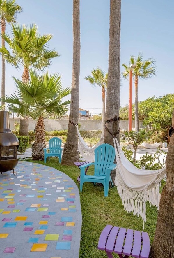 A patio with colorful tiles, two turquoise chairs, a hammock, and a grill.