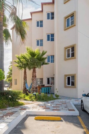 A multi-story residential building with a paved courtyard, palm trees, and a car parked in front.