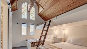 Quarto com teto estilo loft, duas camas, escada e janela com design em vitral.