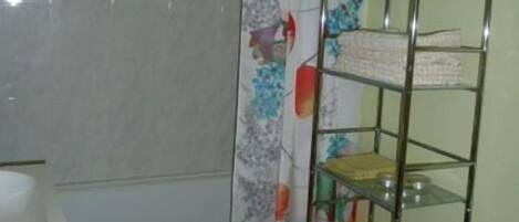 Un baño con inodoro, lavamanos, cortina de ducha con estampado floral y un estante metálico con recipientes amarillos.
