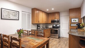 A compact kitchen with wooden cabinets, a microwave, a stove, and a dining table with chairs. - Tamarack - Steps to the Slopes + ASE Transportation (Snowmass Village)