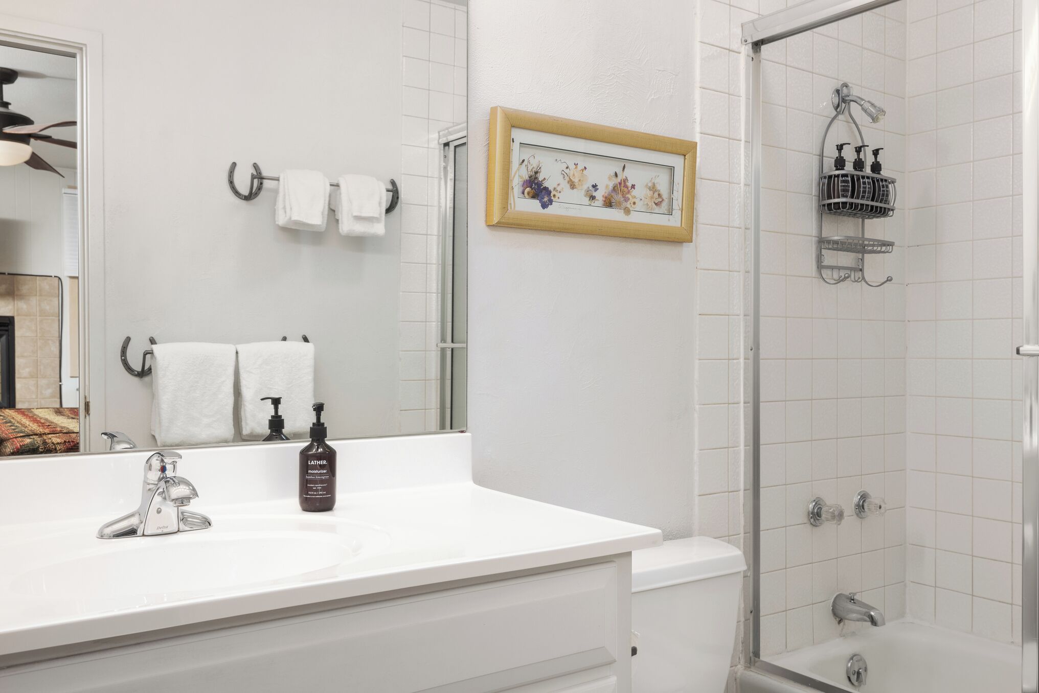 A bathroom with a white sink, a mirror, a framed picture on the wall, and a shower area.