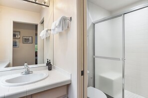 Een badkamer met een wit wastafelmeubel, spiegel en een douchecabine met glazen wanden.