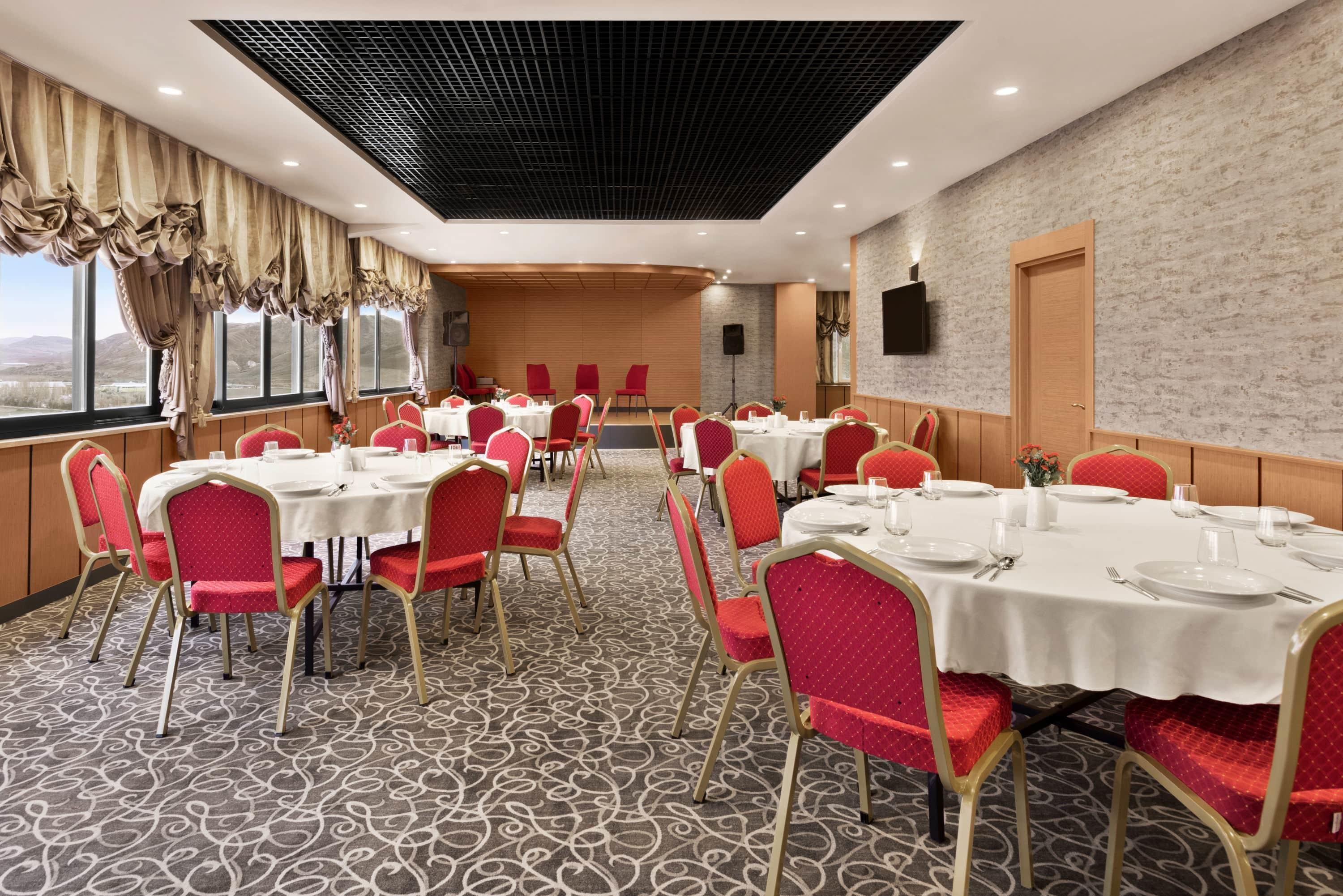 A conference room with multiple tables and chairs, large windows, and a high ceiling with a grid pattern.