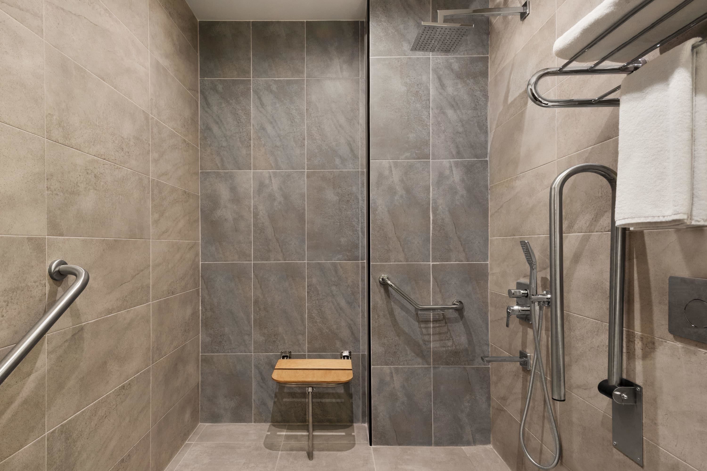 A shower area with a handrail, a small wooden bench, and a towel rack.