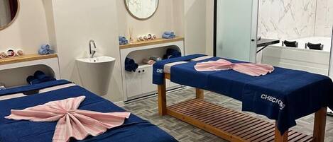 A spa room with two massage tables, a sink, and a mirror.