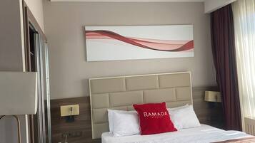 A hotel room with a bed, a nightstand, a lamp, a wall-mounted artwork, and a window with curtains.