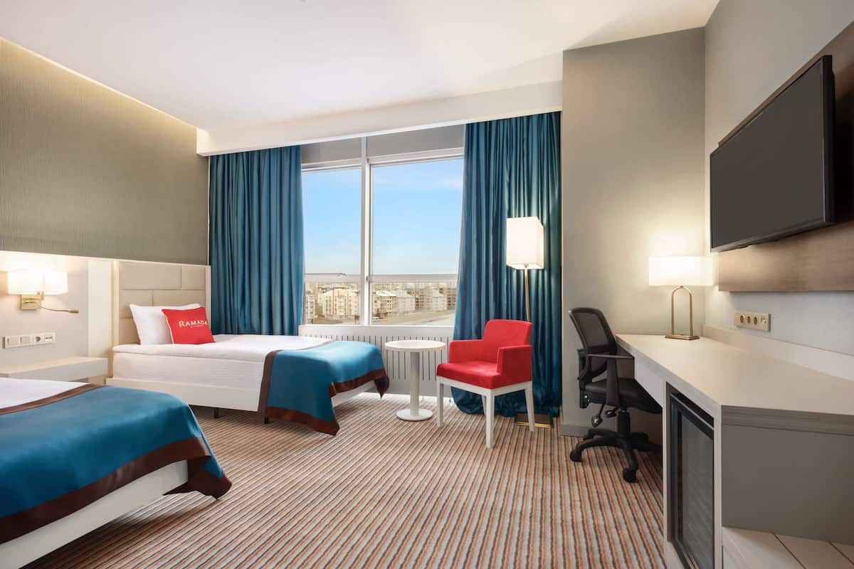 Une chambre d’hôtel avec deux lits, un bureau, une chaise, une télévision et une fenêtre avec des rideaux.