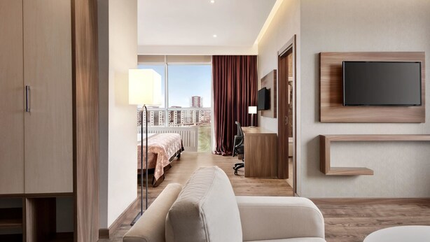 Una habitación de hotel moderna con una cama grande, un sofá, un escritorio y un televisor fijado a la pared.