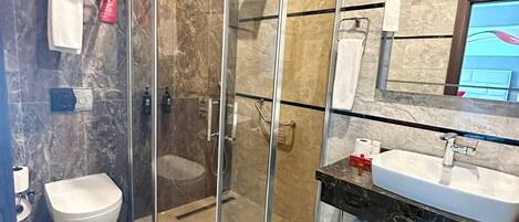 Un baño moderno con ducha de vidrio, inodoro y tocador con lavamanos.