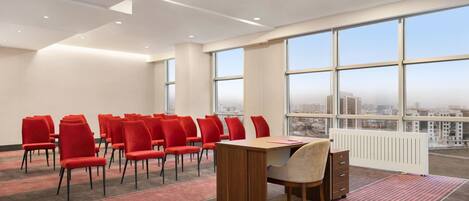 A conference room with red chairs, a wooden table, and large windows with a city view.