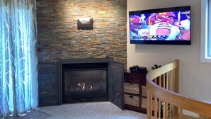 A living room with a stone fireplace, a flat-screen TV mounted above it, and a wooden chair. - NordicVillageRESORT life@Storyland, very close to Attitash/Wildcat/Cranmore etc (Jackson)