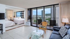 Una habitación de hotel con balcón, una cama, un sofá y una mesa de centro de vidrio.