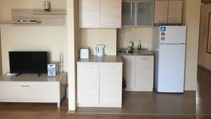 A compact kitchen with a built-in refrigerator, a coffee maker, and a toaster. There is a small shelf above the counter and a television on a stand. - Budzhaka Black Sea Paradise (Sozopol)