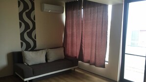 A room with a dark-colored sofa, a patterned wall, and a window with curtains. - Budzhaka Black Sea Paradise (Sozopol)
