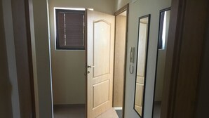 A hallway with a wooden door, a window with blinds, and a mirror on the wall. - Budzhaka Black Sea Paradise (Sozopol)