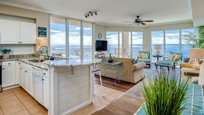 Une cuisine spacieuse avec un grand îlot central, un coin repas offrant une vue sur l’océan et un salon doté de sièges confortables et d’un ventilateur de plafond.