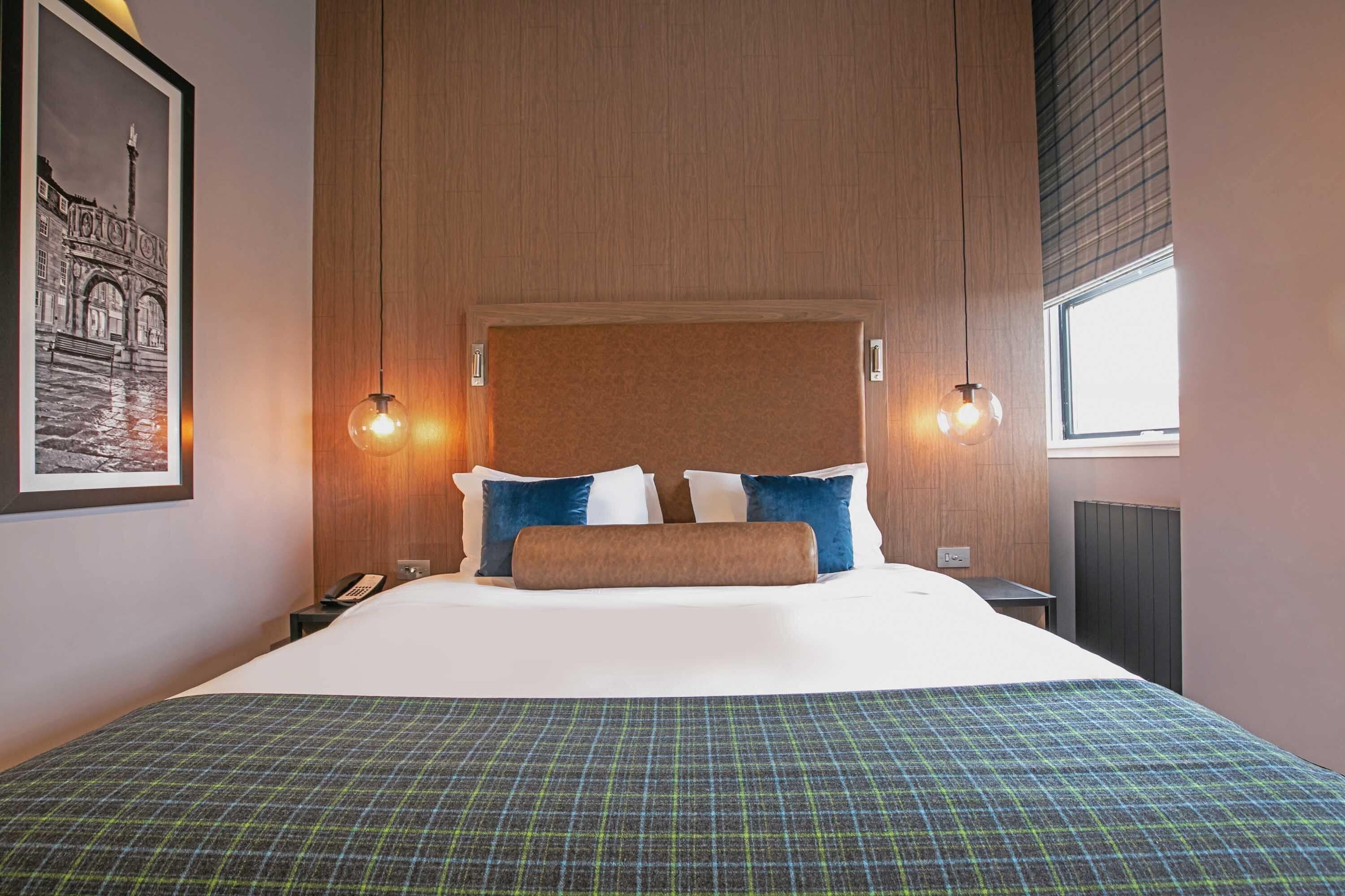 A hotel room with a large bed, two bedside lamps, a framed picture on the wall, and a window with blinds.