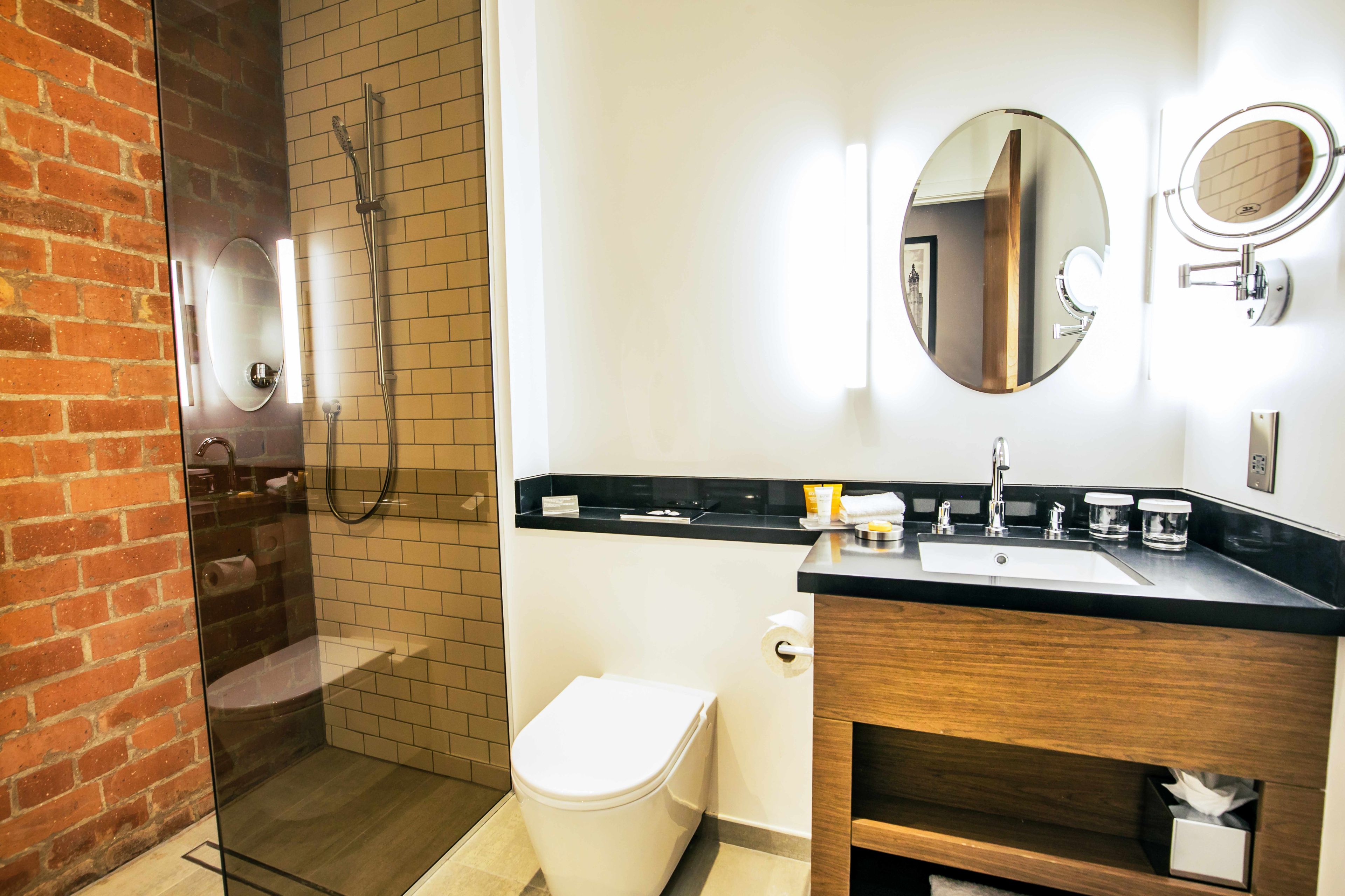 Et moderne badeværelse med en brusekabine i glas, et hvidt toilet og en sort kommode med spejl.