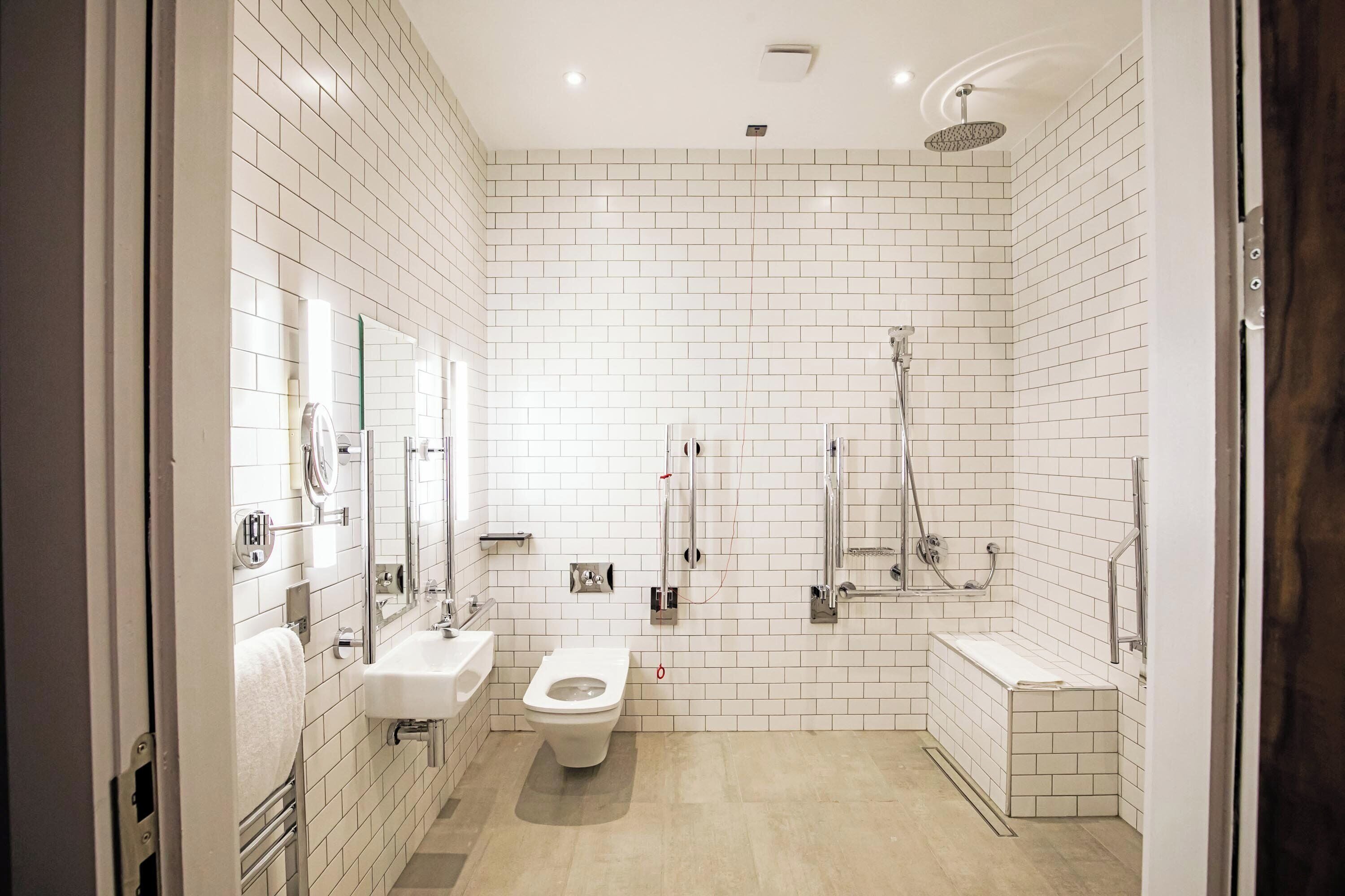 A modern bathroom with white tiled walls, a toilet, a sink, and a shower area.