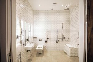 Un baño moderno con paredes de azulejos blancos, un inodoro, un lavabo y una zona de ducha.